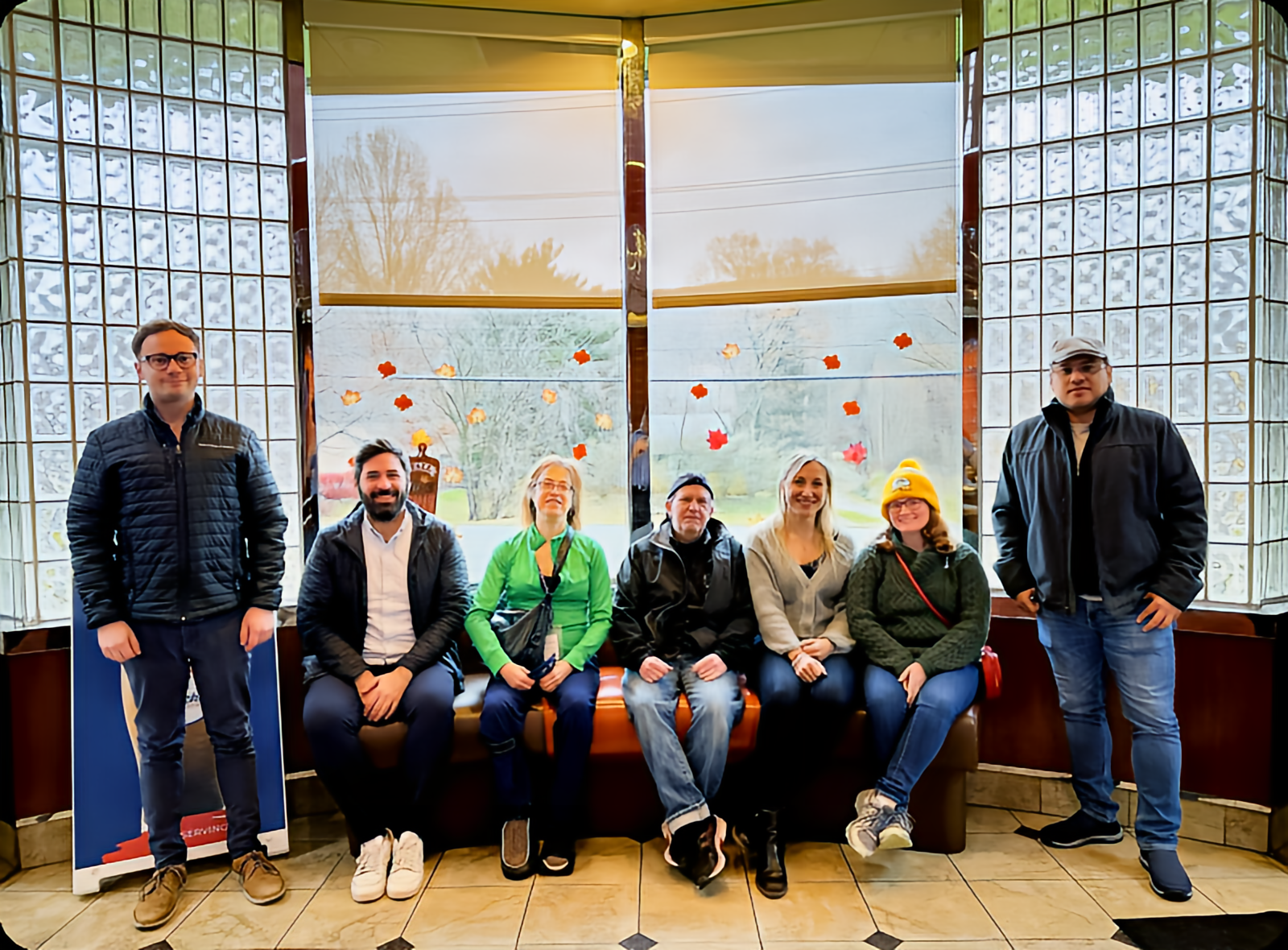 Seven people sitting on a bench indoors.